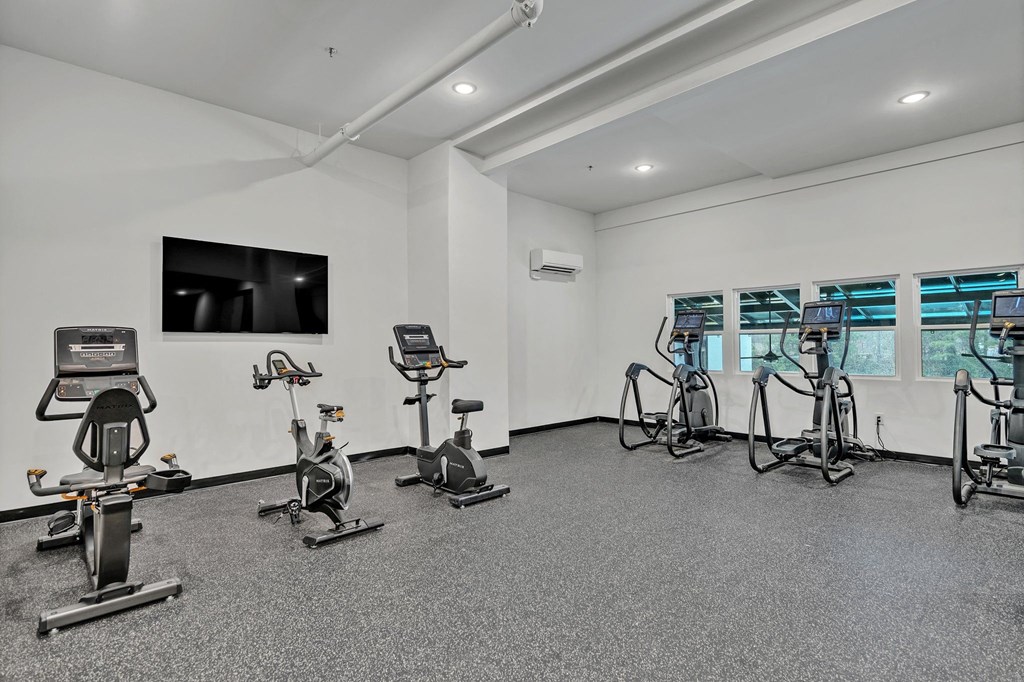 A room with a grey floor and white walls has a row of exercise bikes.