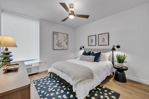 A bedroom with a bed, a ceiling fan, and two wall lamps.