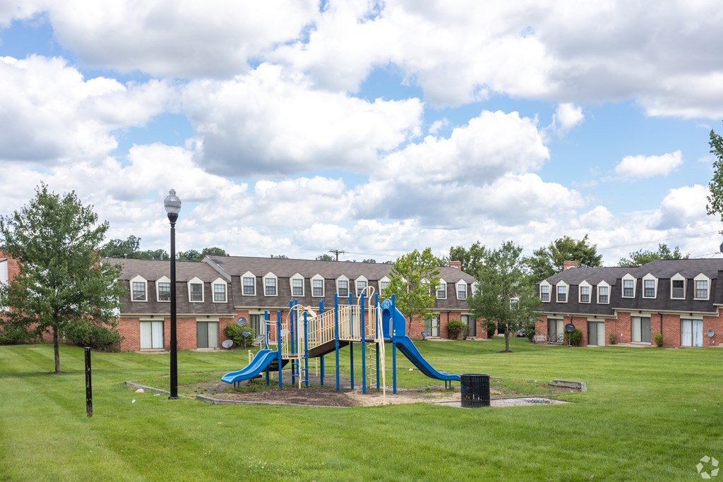 A playground with a blue slide in the middle of a grassy area.