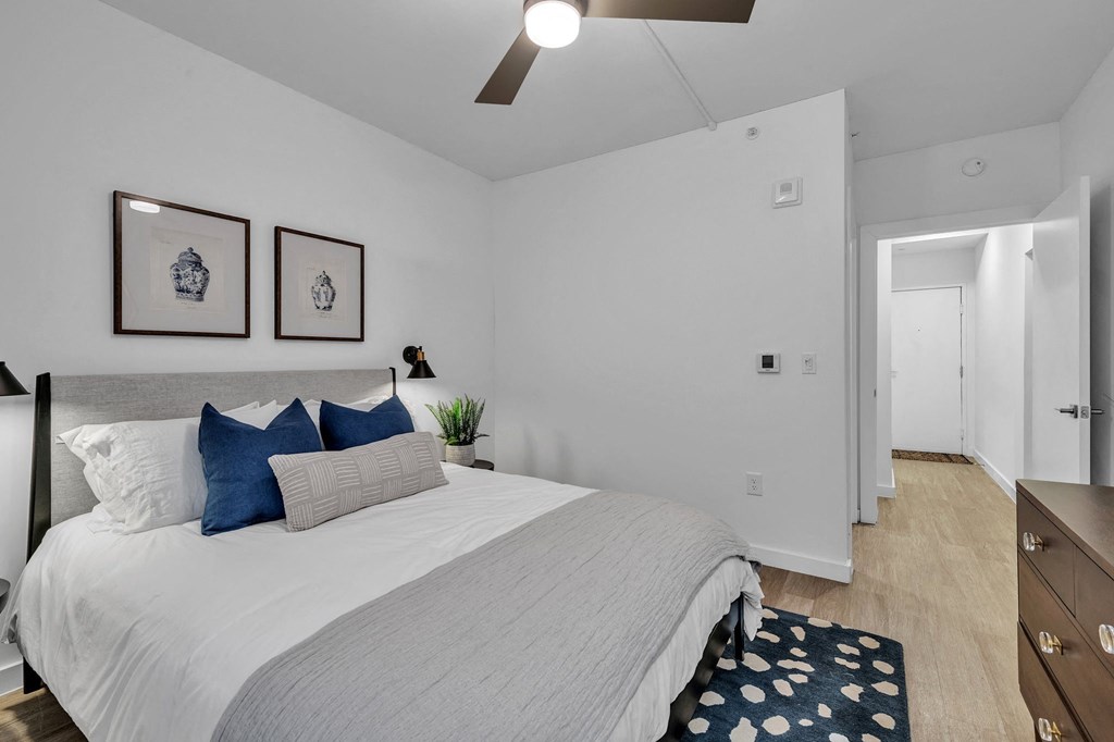 A bedroom with a bed, two pillows, a ceiling fan, and two pictures on the wall.