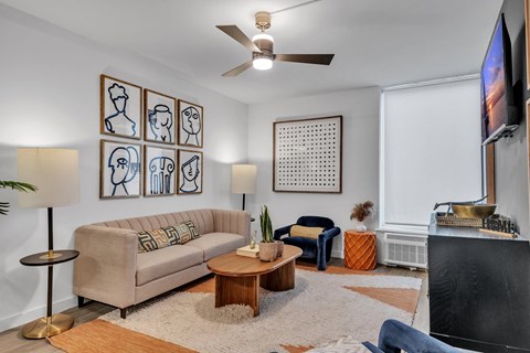 A living room with a beige couch, a wooden coffee table, and a television on the wall.