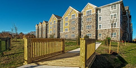 A wooden gate leads to a grassy area in front of a large apartment building.
