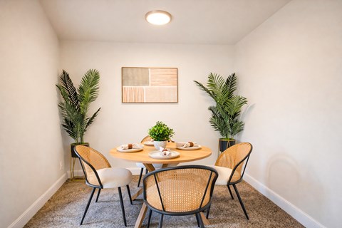 A dining room with a table set for two and a plant on each side.