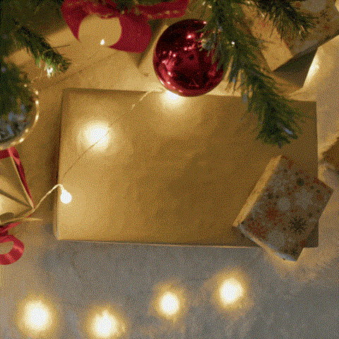 A red Christmas ornament hangs on a tree branch above a wrapped present.