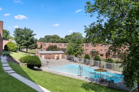 A pool surrounded by a fence and trees in front of a brick building.