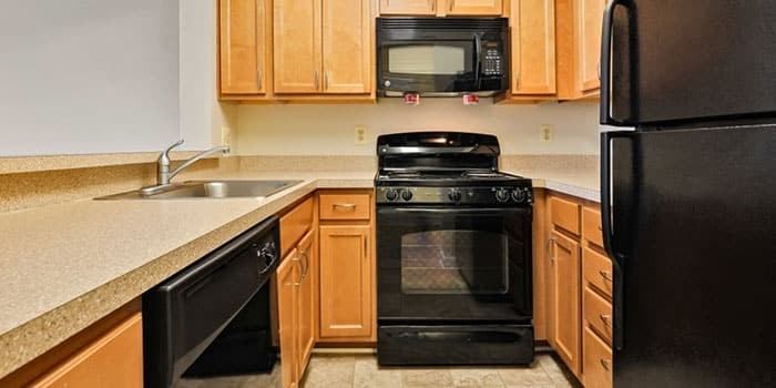 A black stove top oven sits in a kitchen with wooden cabinets. at Rainier Manor Apartments, Maryland, 20712