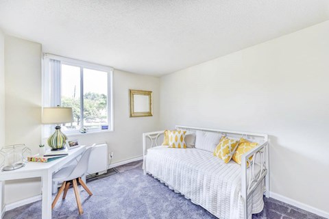 A bedroom with a white bed and a desk with a lamp.