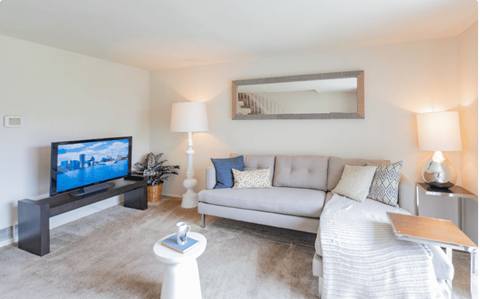 A living room with a grey couch, a white coffee table, and a television on a stand at Dutch Village Apartments, Maryland 21234