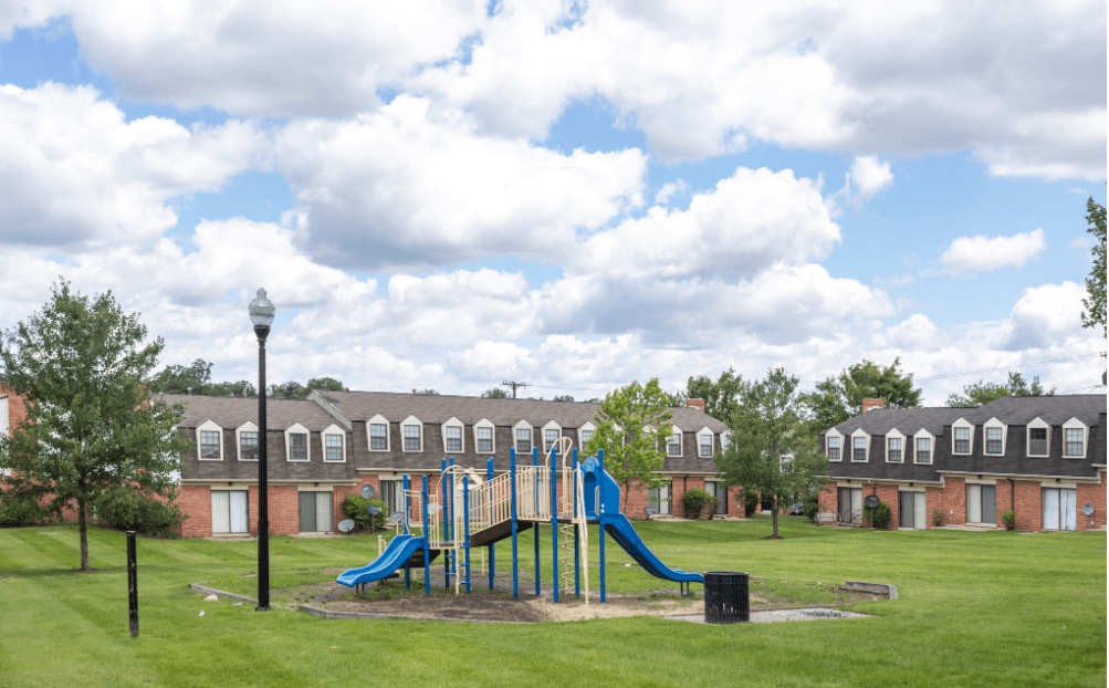 A playground with a blue slide and a green slide in the middle of a grassy area. A playground with a blue slide and a green slide in the middle of a grassy area at Dutch Village Apartments, Baltimore, Maryland