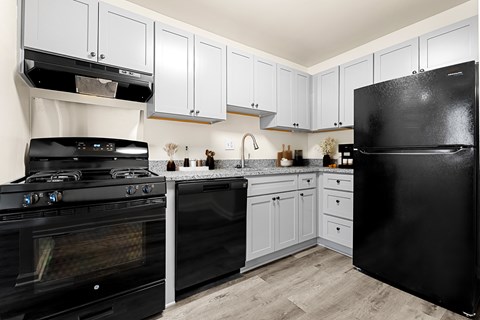 A black refrigerator sits in a kitchen with white cabinets.