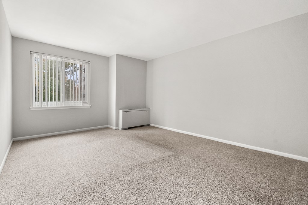 A room with a carpeted floor and a window with blinds.