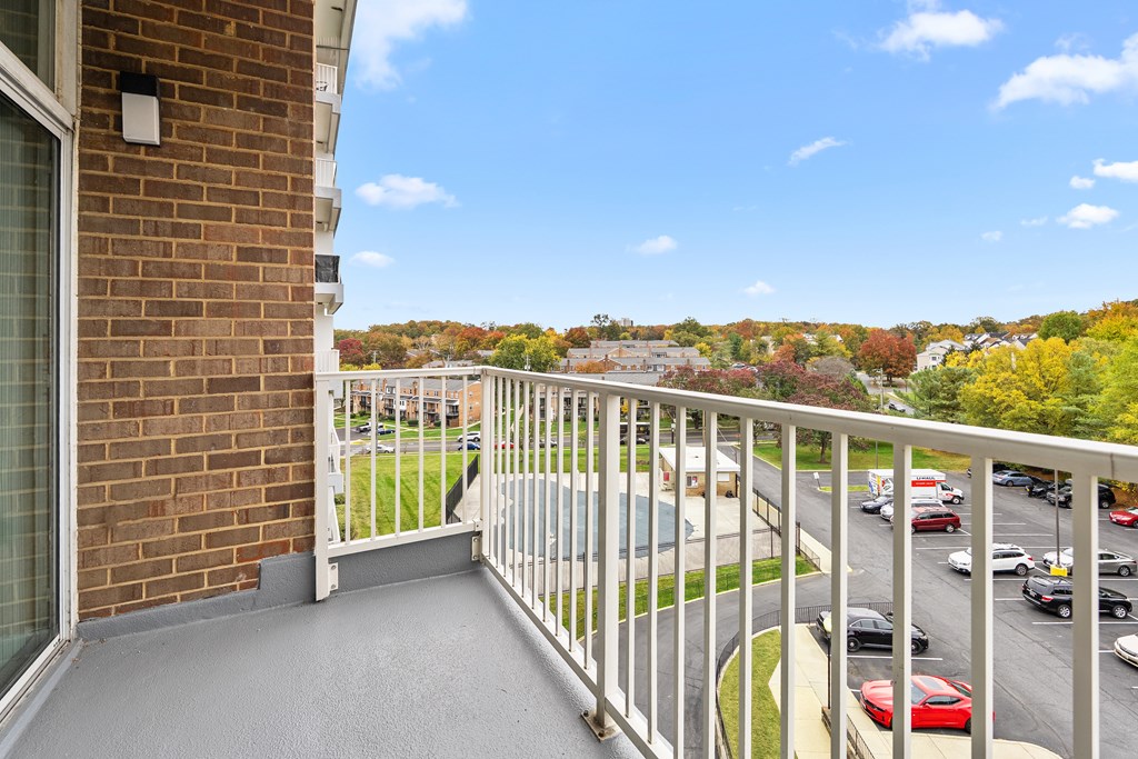 A balcony with a view of a parking lot and trees.