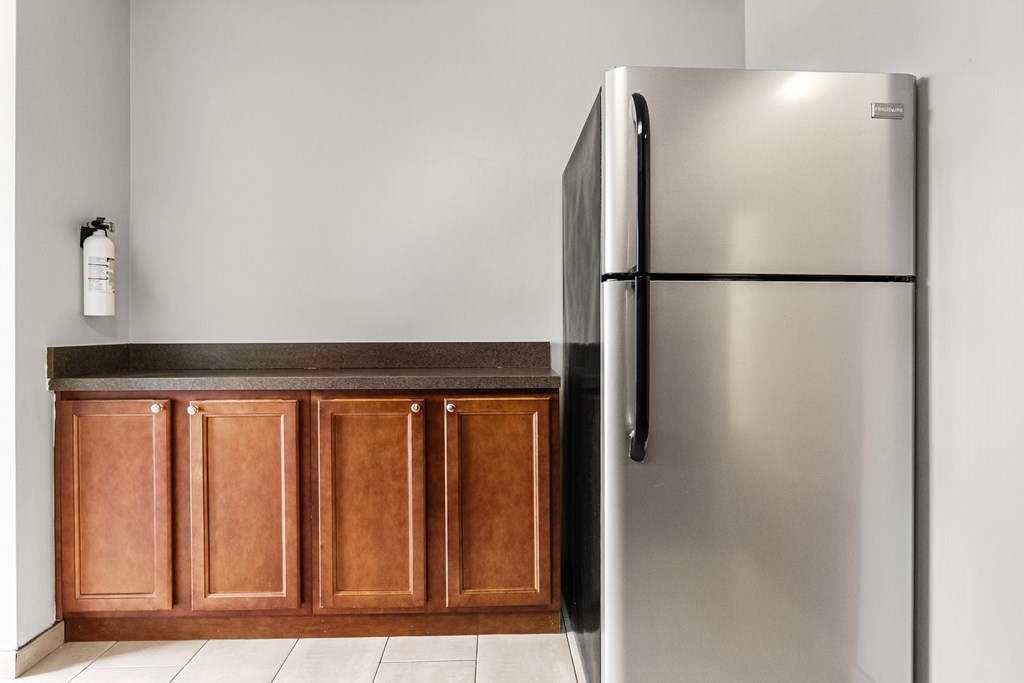 A stainless steel refrigerator stands next to a wooden cabinet in a kitchen.