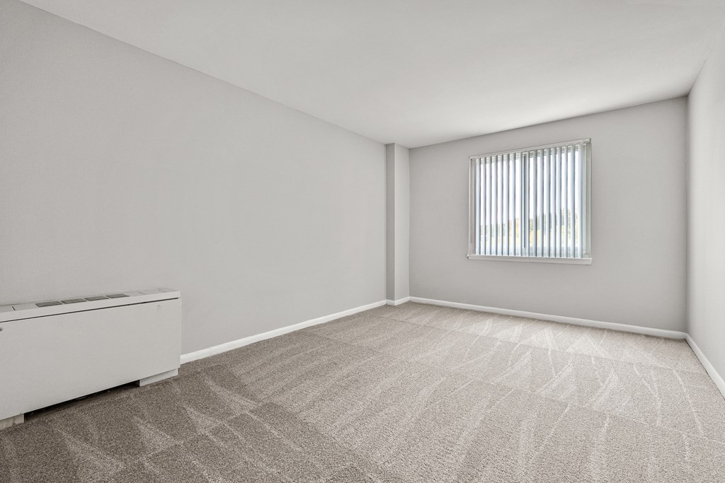 A room with a carpeted floor and a window with blinds.