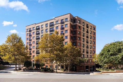 A large brick building with many windows and balconies is surrounded by trees.