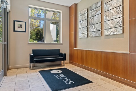A black sofa sits in front of a window in a room with a black doormat that says "ROSS".