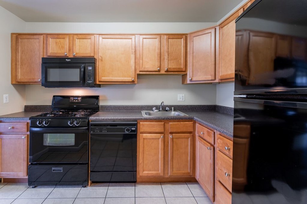 A kitchen with black appliances and wooden cabinets at Charlestowne North Apartments, Greenbelt, Maryland