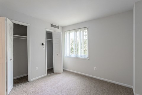 A white bedroom with a window and a carpeted floor at Charlestowne North Apartments, Greenbelt
