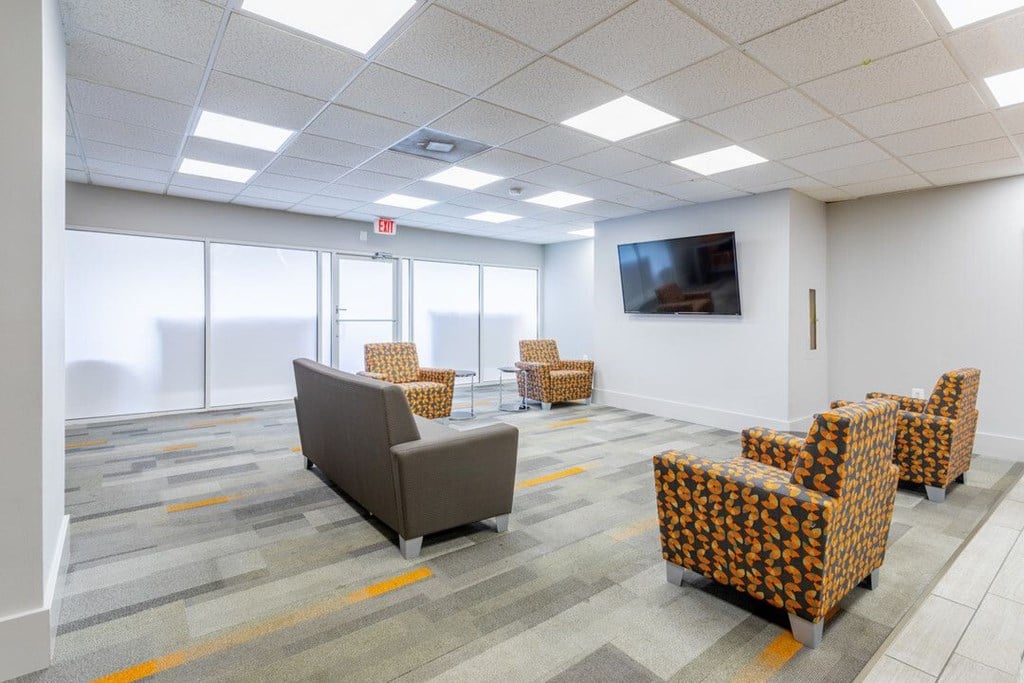 A conference room with a grey sofa, orange patterned chairs, and a television on the wall at Charlestowne North Apartments, Maryland