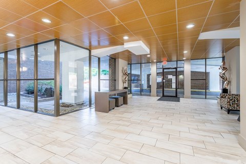 A spacious hallway with a tiled floor and glass walls leading to an outdoor area at Charlestowne North Apartments, Greenbelt, MD
