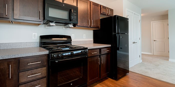 A black refrigerator sits in a kitchen with dark wood cabinets. at Rainier Manor Apartments, Mount Rainier, MD, 20712