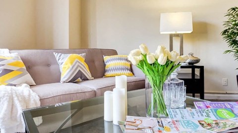 A living room with a grey couch, a glass table, and a vase of white flowers at Ashton Heights Apartments, Maryland, 20746