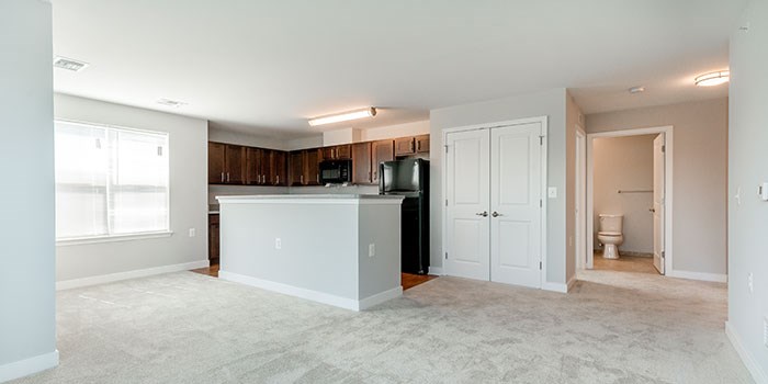 A spacious living room with a kitchenette and a bathroom visible in the background. at Rainier Manor Apartments, Mount Rainier, MD