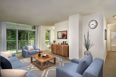 A living room with a blue sofa, a wooden coffee table, and a large window with a view of trees at Charlestowne North Apartments, Maryland, 20770