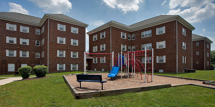 A playground with a slide and a bench in front of a red brick building.