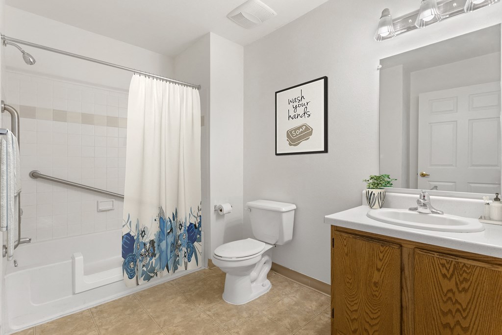 bathroom at Creekside at Taskers Chance in Frederick, MD with wood vanity with white countertops, white tub, tan tile floor and mirror with vanity lights