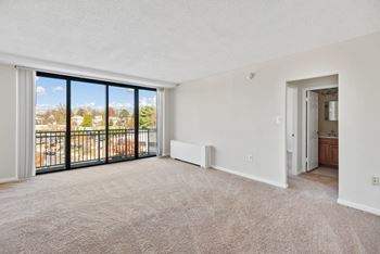 A spacious living room with a view of a parking lot through the sliding glass doors at The Brittany, Washington, DC, 20015
