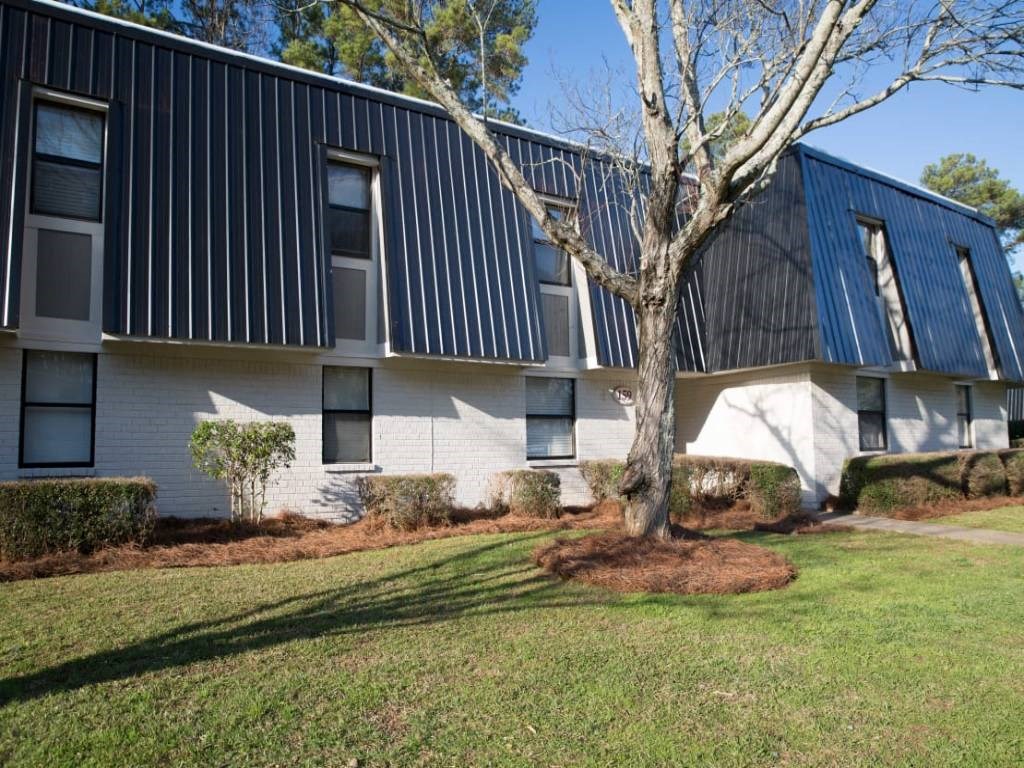 a white building with a blue roof and a tree in the yard