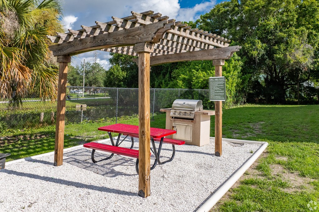 A picnic area with a red table and a wooden pergola.
