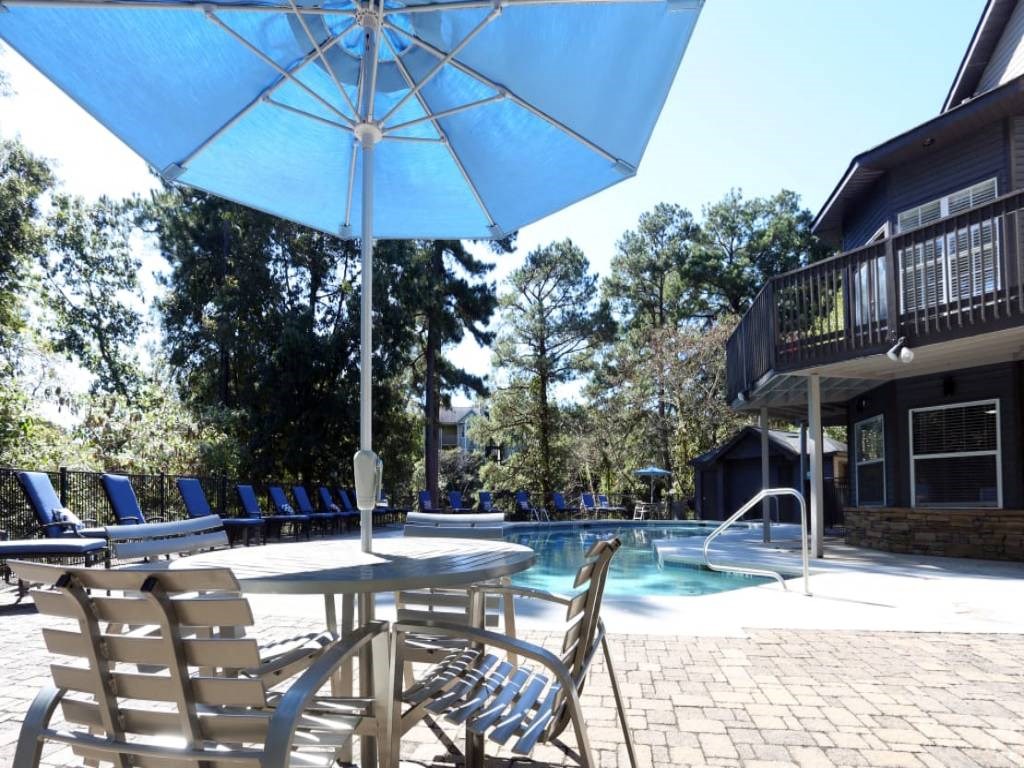 a patio with chairs and an umbrella next to a pool