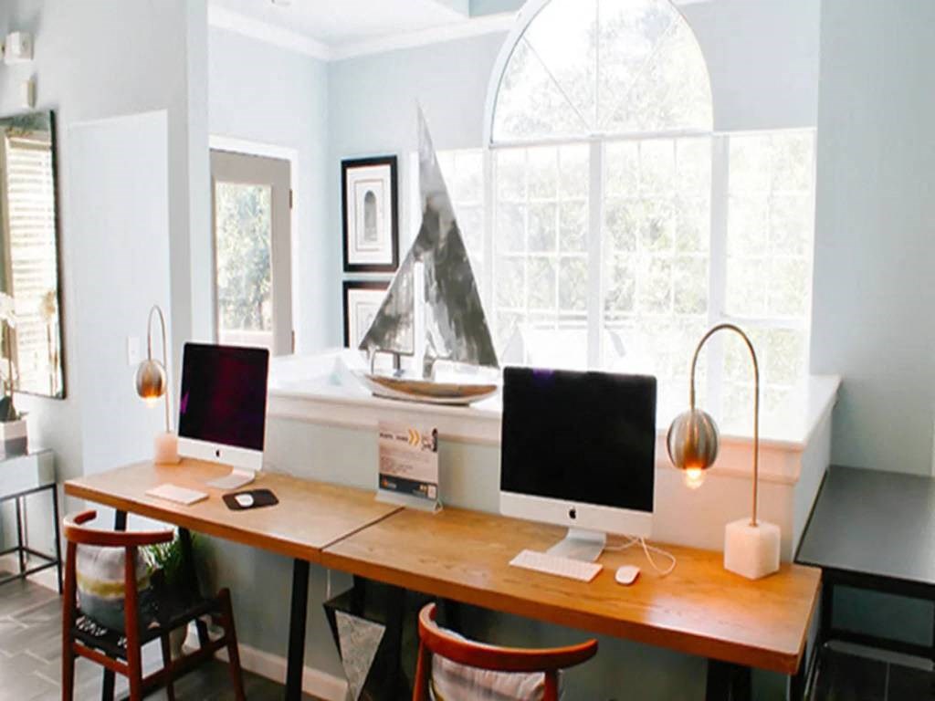 a home office with two computer monitors and a sailboat in the window
