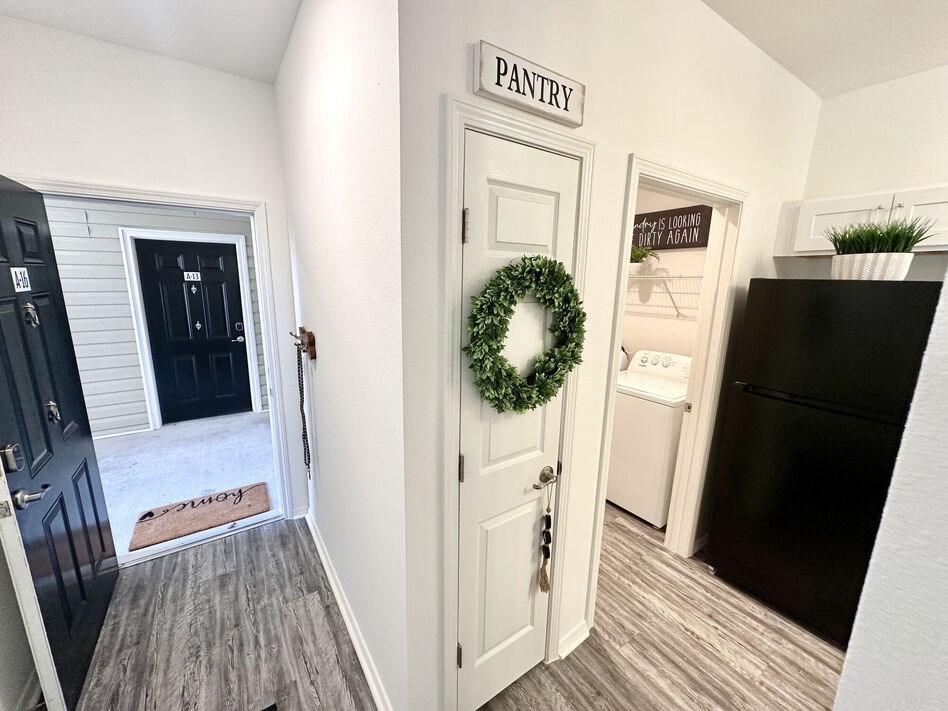 A black fridge sits in a kitchen next to a door with a wreath on it.