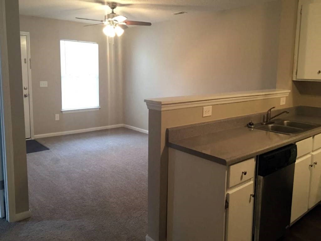 an empty living room with a kitchen and a ceiling fan