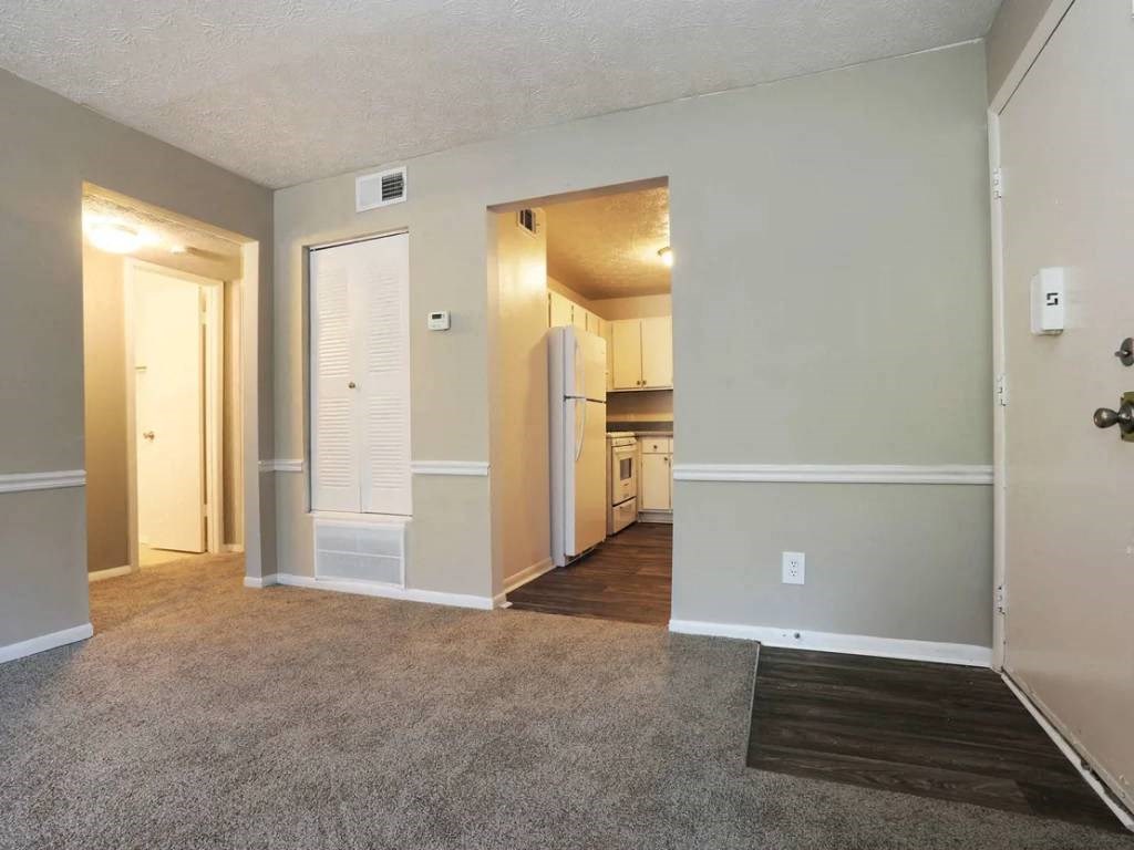 an empty living room with a kitchen in the background