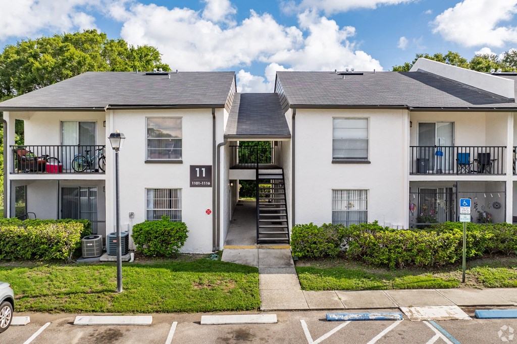 A white two-story apartment building with a black roof and a parking lot in front.