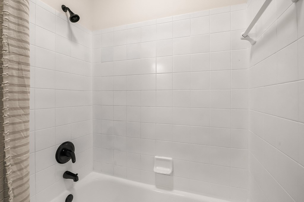 A white tiled shower with a black faucet and a white tub.