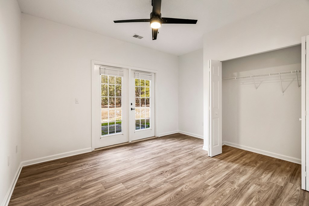 A room with a ceiling fan and a large window with a view of a building.