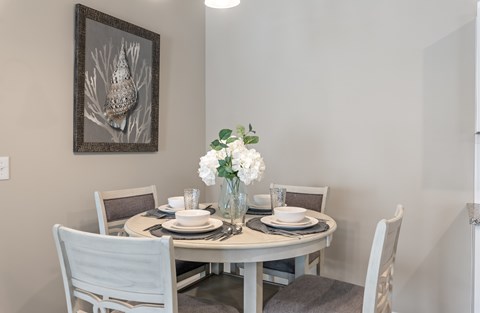A dining table set with plates and glasses with a vase of white flowers on top.