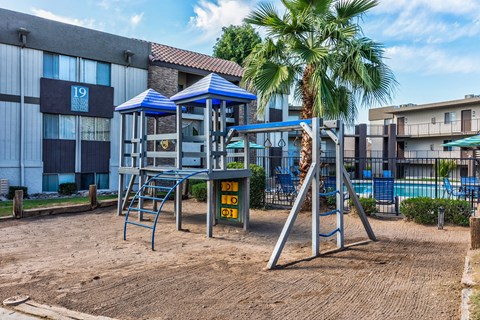 A playground with a blue canopy and a palm tree in the background.