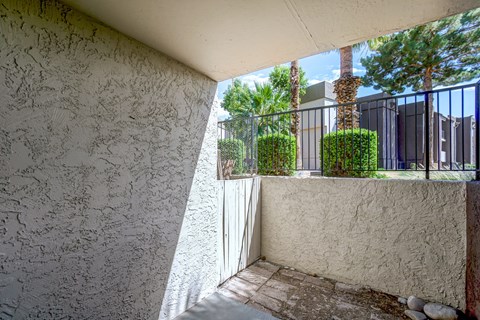 A patio area with a white wall and a view of a fence and trees.