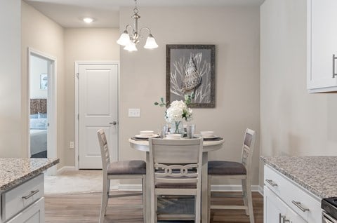 A kitchen with a table set for two with a vase of flowers on it.