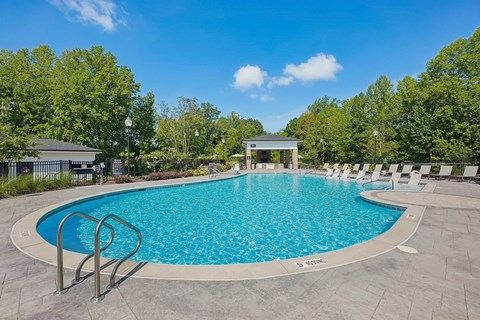 A large outdoor swimming pool surrounded by trees and a pavilion.