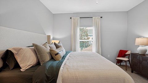 A bedroom with a large bed and a chair by the window.
