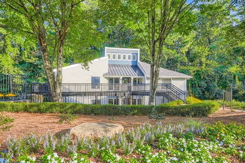A house with a grey roof and a blue window is surrounded by green trees and bushes.