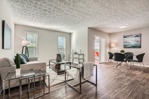 A living room with a grey couch, a glass coffee table, and a white rug.