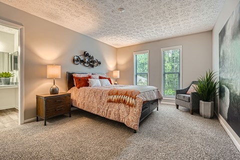 A bedroom with a bed, nightstand, and a plant.